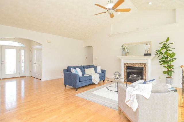 living room featuring a premium fireplace, vaulted ceiling, light hardwood / wood-style flooring, and ceiling fan