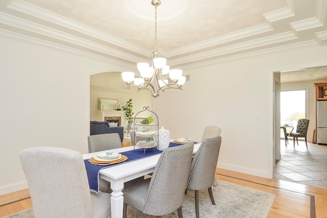 dining room featuring an inviting chandelier, crown molding, a tray ceiling, and light wood-type flooring