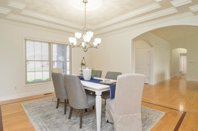 dining area with a notable chandelier, a raised ceiling, wood-type flooring, and crown molding