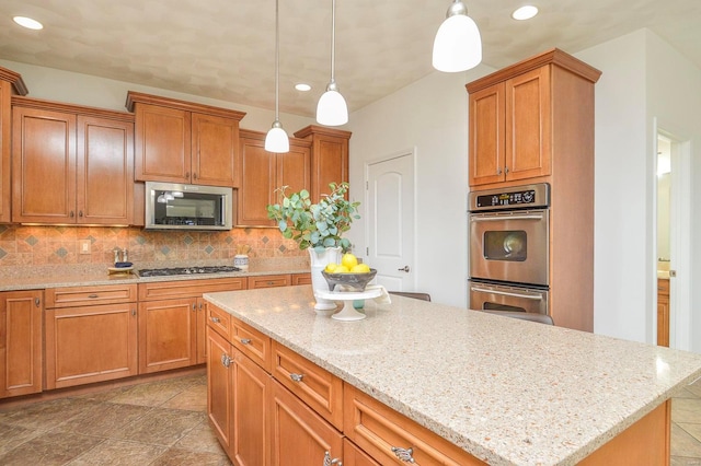 kitchen featuring hanging light fixtures, light stone counters, backsplash, appliances with stainless steel finishes, and a center island