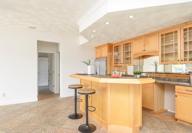 kitchen featuring stainless steel fridge, light brown cabinets, a center island, and a breakfast bar