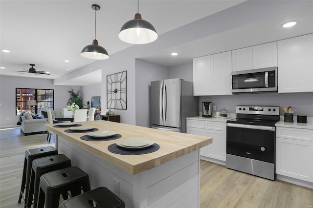 kitchen with appliances with stainless steel finishes, decorative light fixtures, white cabinetry, and light hardwood / wood-style floors