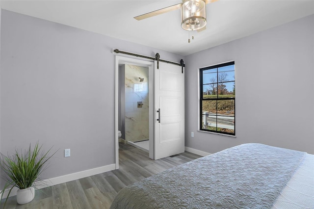 bedroom featuring connected bathroom, a barn door, light wood-type flooring, and ceiling fan