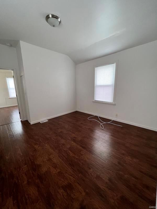 spare room featuring dark wood-type flooring, lofted ceiling, and plenty of natural light