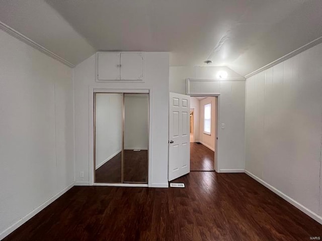 unfurnished bedroom with crown molding, vaulted ceiling, dark hardwood / wood-style floors, and a closet