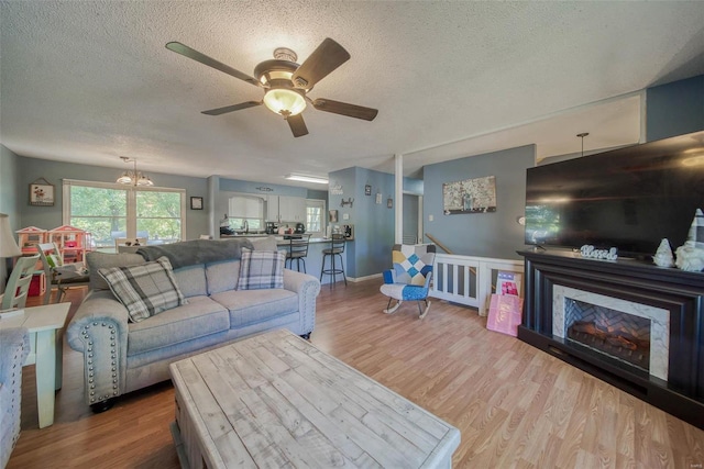 living room featuring a premium fireplace, hardwood / wood-style floors, a textured ceiling, and ceiling fan with notable chandelier