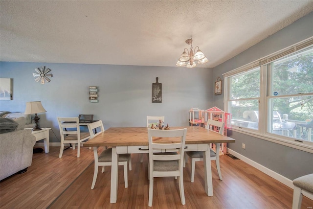 dining area with a textured ceiling, a notable chandelier, and wood-type flooring