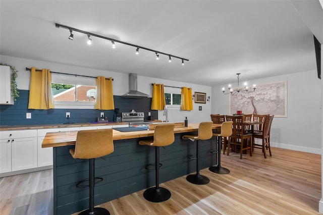 kitchen with white cabinetry, wall chimney range hood, wooden counters, backsplash, and light wood-type flooring