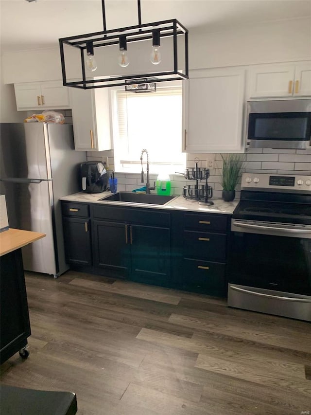 kitchen featuring appliances with stainless steel finishes, sink, white cabinetry, light hardwood / wood-style floors, and decorative backsplash