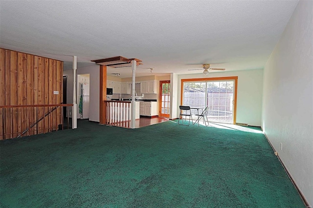 unfurnished living room featuring wood walls, a textured ceiling, carpet flooring, and ceiling fan