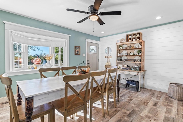 dining room with ceiling fan, wooden walls, and light hardwood / wood-style floors