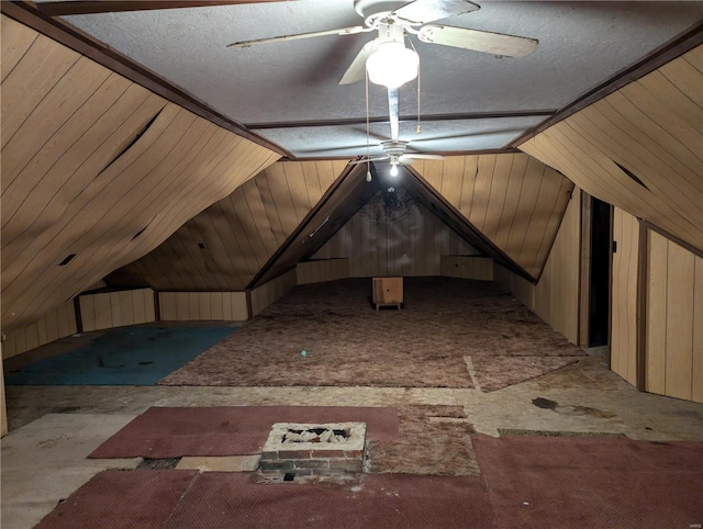 interior space with lofted ceiling, a textured ceiling, wooden walls, and ceiling fan