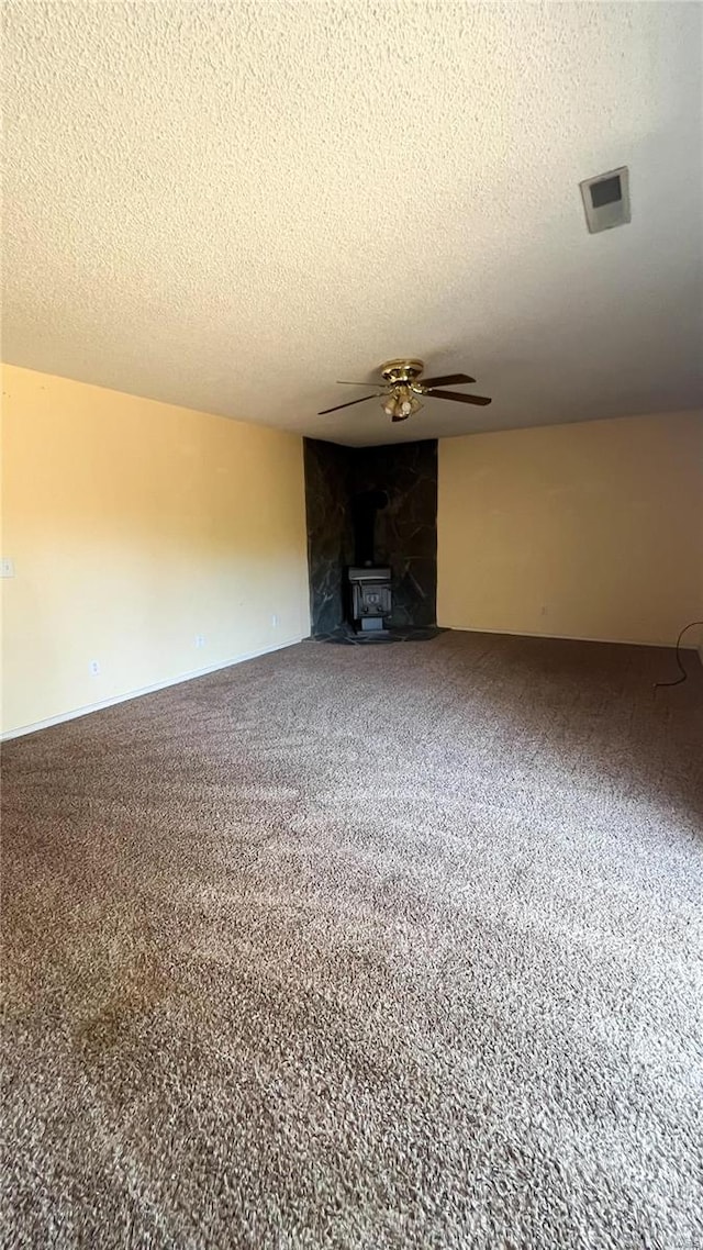 unfurnished living room featuring carpet flooring, a wood stove, a textured ceiling, and ceiling fan