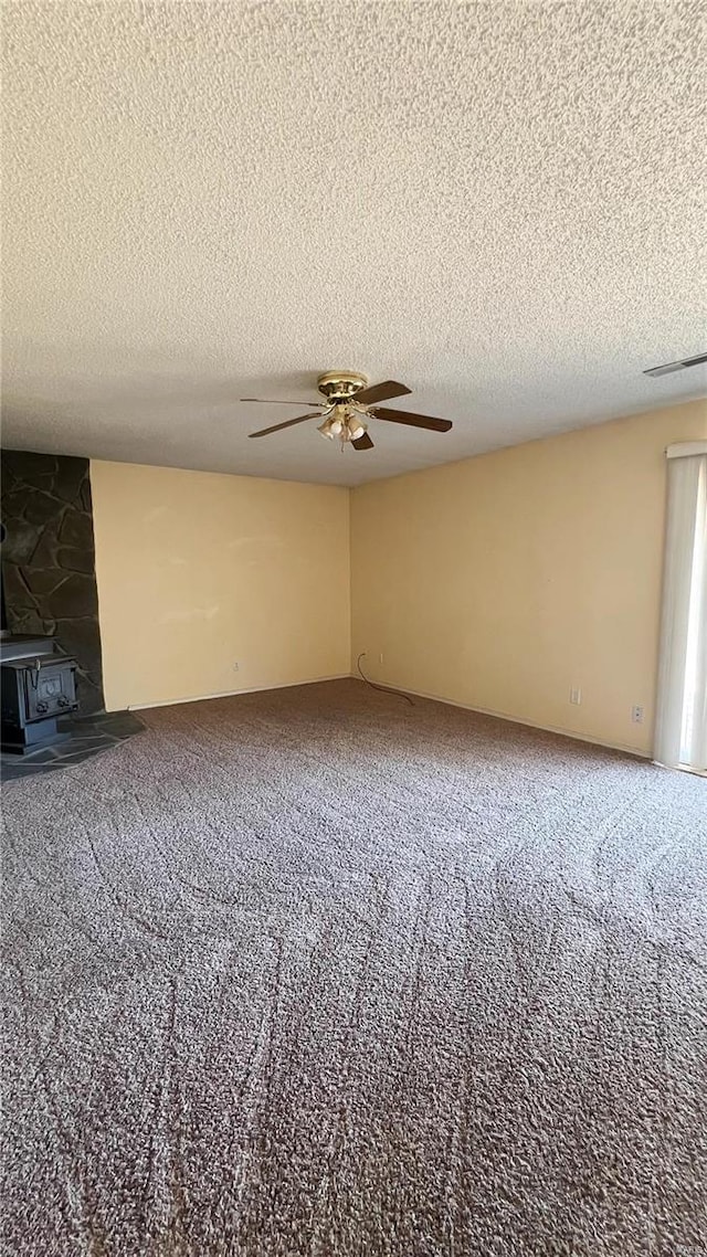 carpeted spare room featuring ceiling fan, a wood stove, and a textured ceiling