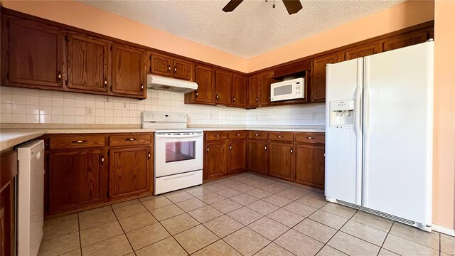 kitchen with a textured ceiling, light tile patterned floors, backsplash, and white appliances