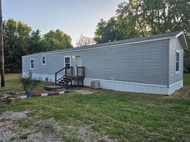 rear view of house featuring central air condition unit and a lawn