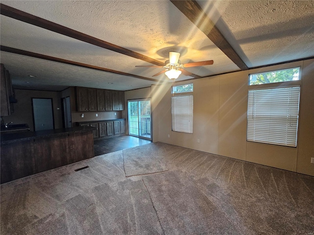 unfurnished living room with a textured ceiling, beamed ceiling, dark carpet, and ceiling fan