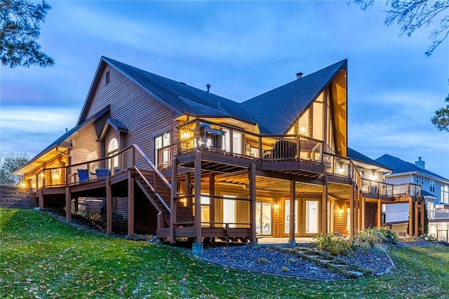 back house at dusk with a balcony, a yard, and a deck