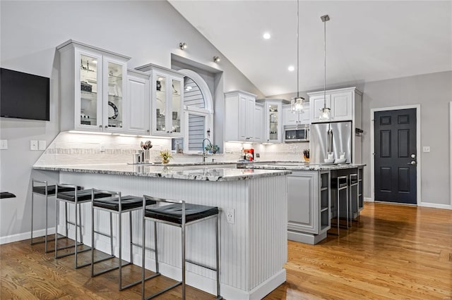 kitchen featuring stainless steel appliances, light stone countertops, white cabinets, decorative light fixtures, and kitchen peninsula