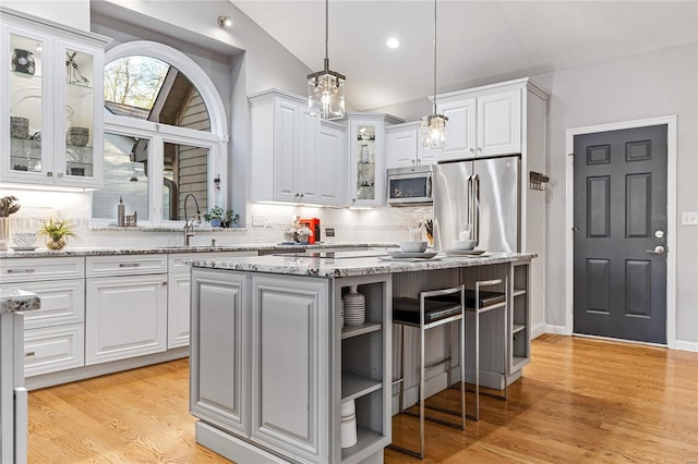 kitchen featuring a kitchen island, pendant lighting, white cabinetry, stainless steel appliances, and light stone countertops