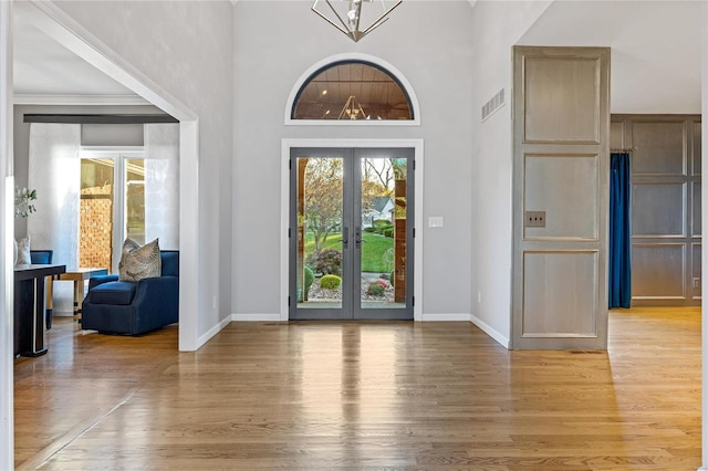 foyer entrance featuring a towering ceiling, light wood-type flooring, and french doors