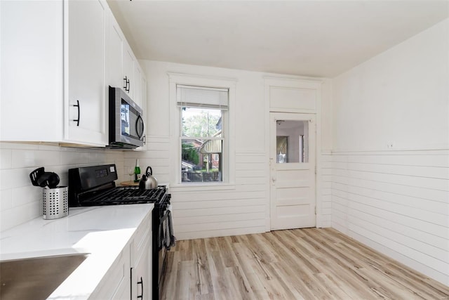 kitchen with light hardwood / wood-style floors, black gas range oven, and white cabinets