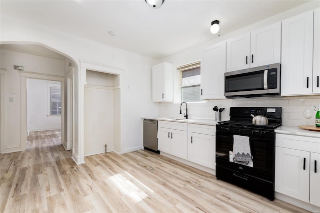 kitchen featuring appliances with stainless steel finishes, sink, white cabinets, decorative backsplash, and light hardwood / wood-style flooring