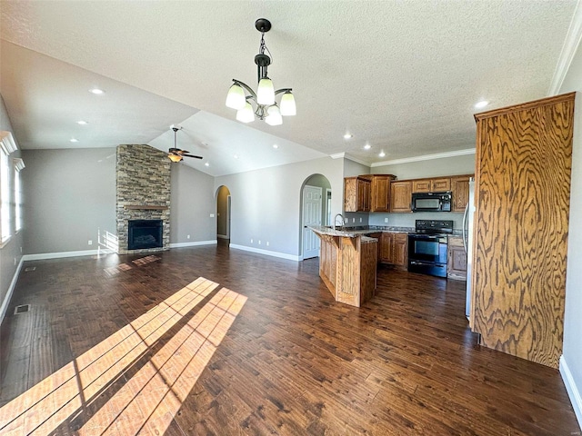 kitchen featuring black appliances, a stone fireplace, vaulted ceiling, dark wood-type flooring, and a breakfast bar area