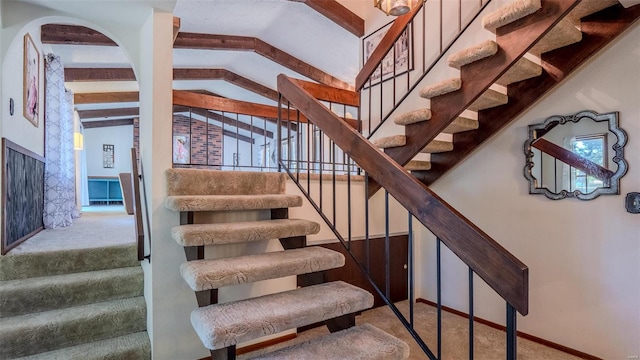 staircase featuring carpet floors and vaulted ceiling with beams