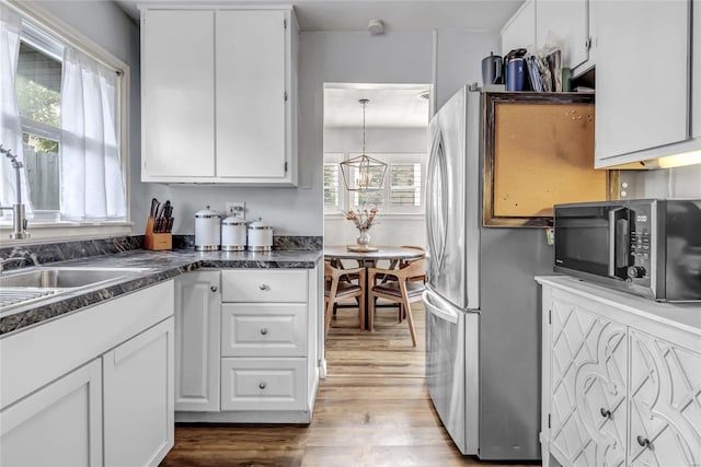 kitchen with white cabinets, an inviting chandelier, stainless steel refrigerator, pendant lighting, and light hardwood / wood-style floors