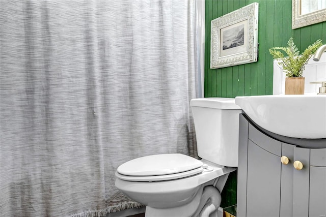 bathroom featuring toilet, wood walls, and vanity