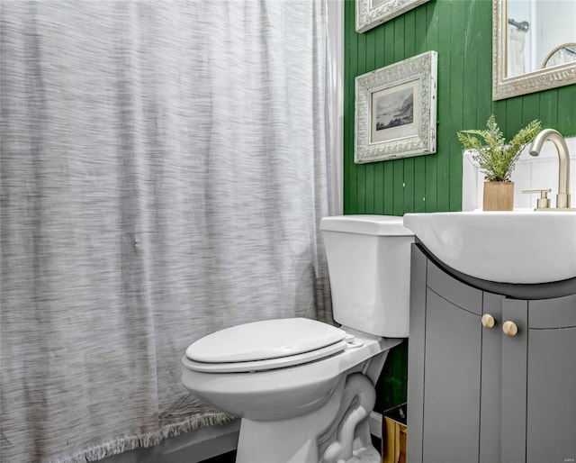 bathroom with toilet, wood walls, and vanity