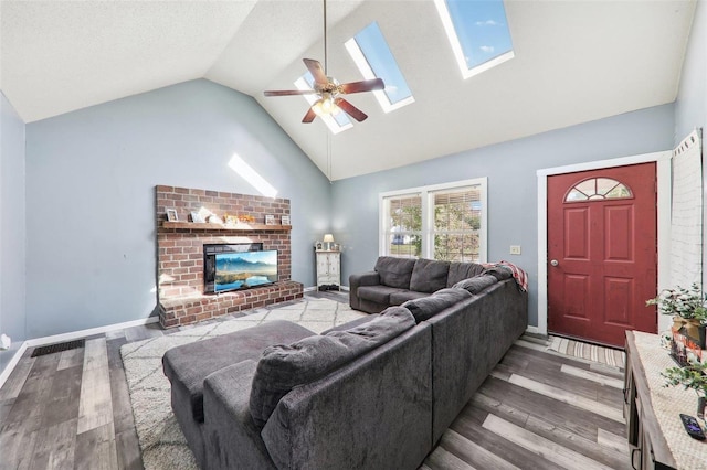 living room with hardwood / wood-style floors, a skylight, a fireplace, high vaulted ceiling, and ceiling fan