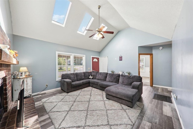 living room featuring hardwood / wood-style floors, a skylight, a fireplace, high vaulted ceiling, and ceiling fan