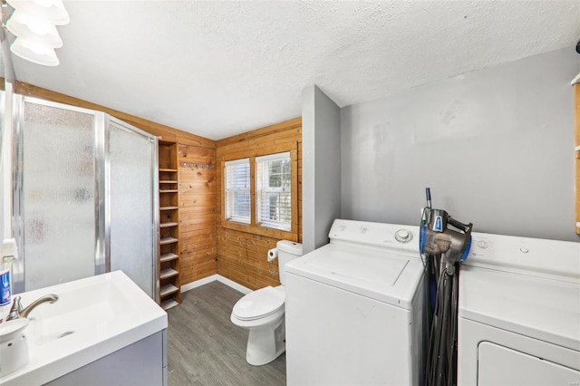 laundry area with hardwood / wood-style floors, wooden walls, washing machine and clothes dryer, and a textured ceiling