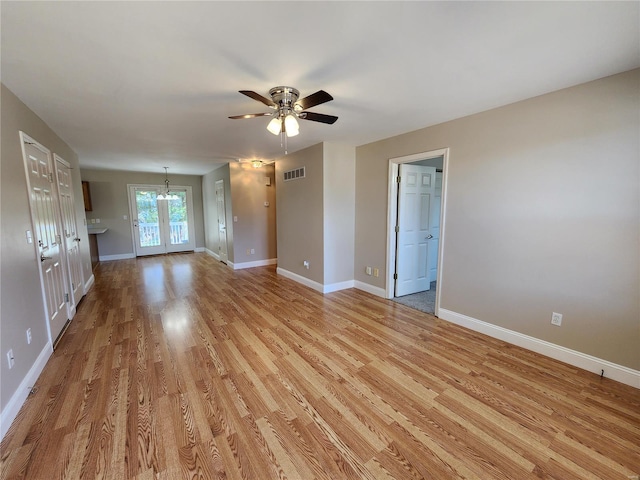 empty room with french doors, light hardwood / wood-style flooring, and ceiling fan with notable chandelier