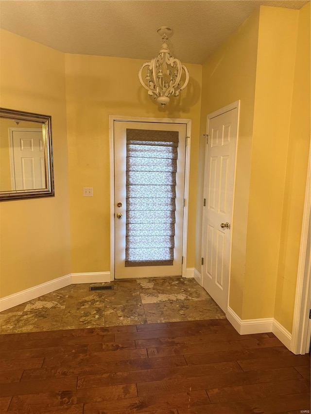 doorway to outside featuring a notable chandelier, a textured ceiling, and dark hardwood / wood-style floors