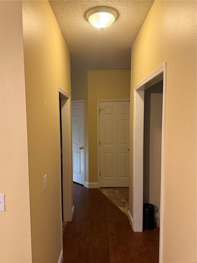 corridor with a textured ceiling and dark hardwood / wood-style flooring