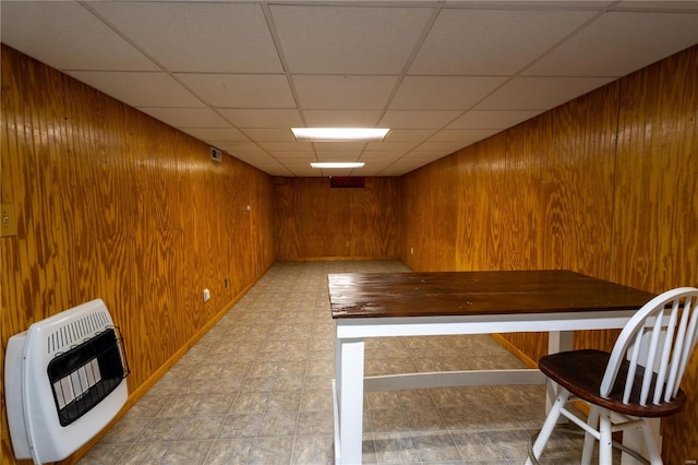 basement with a paneled ceiling, heating unit, and wooden walls