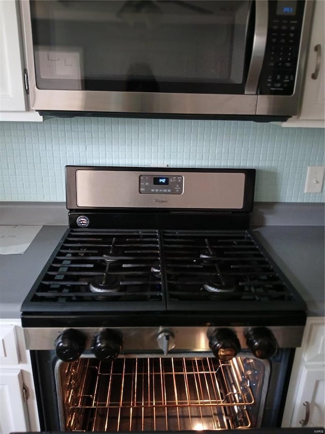 room details with decorative backsplash, white cabinets, and stainless steel appliances