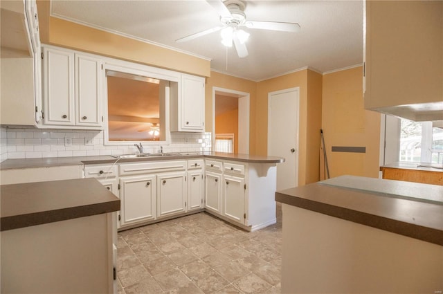 kitchen with kitchen peninsula, ceiling fan, backsplash, white cabinetry, and sink