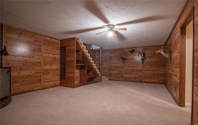 unfurnished living room featuring light carpet, wood walls, a textured ceiling, and ceiling fan