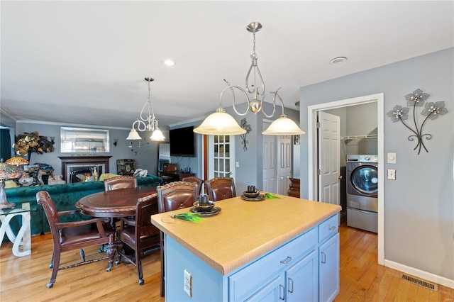 kitchen featuring washer / clothes dryer, hanging light fixtures, a center island, blue cabinets, and light hardwood / wood-style floors