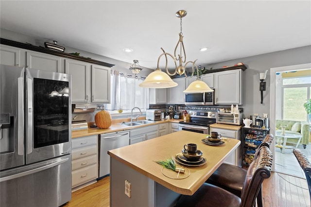 kitchen featuring sink, a kitchen island, light hardwood / wood-style floors, stainless steel appliances, and decorative light fixtures