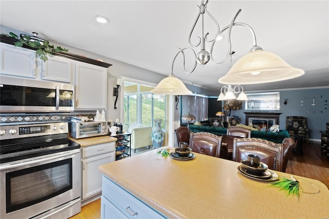 kitchen featuring tasteful backsplash, appliances with stainless steel finishes, white cabinetry, decorative light fixtures, and light hardwood / wood-style flooring