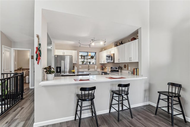 kitchen with kitchen peninsula, a kitchen bar, stainless steel appliances, hardwood / wood-style floors, and white cabinetry