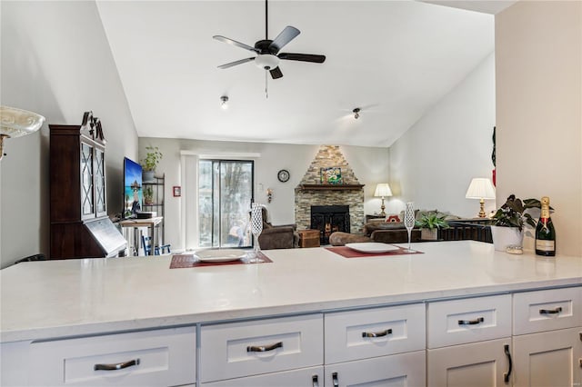 kitchen with white cabinets, ceiling fan, a stone fireplace, and vaulted ceiling