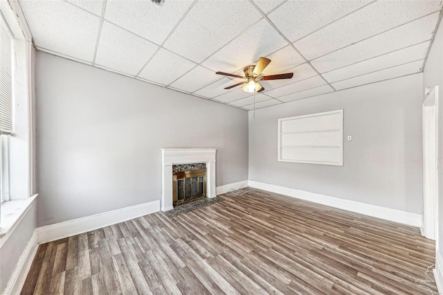 unfurnished living room featuring a drop ceiling, wood-type flooring, and ceiling fan