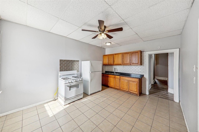 kitchen featuring sink, light tile patterned flooring, a paneled ceiling, white appliances, and tasteful backsplash