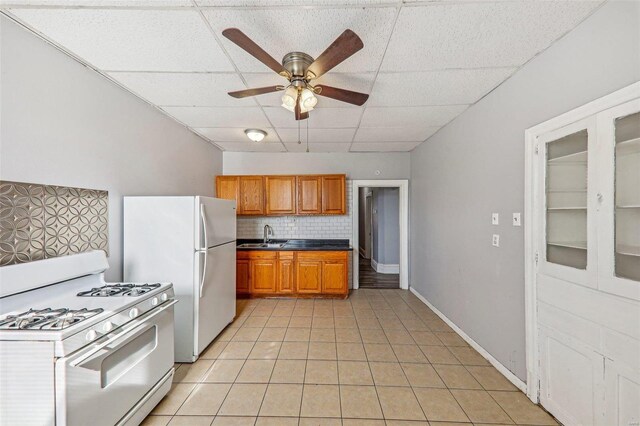 kitchen featuring a drop ceiling, light tile patterned flooring, tasteful backsplash, white appliances, and ceiling fan